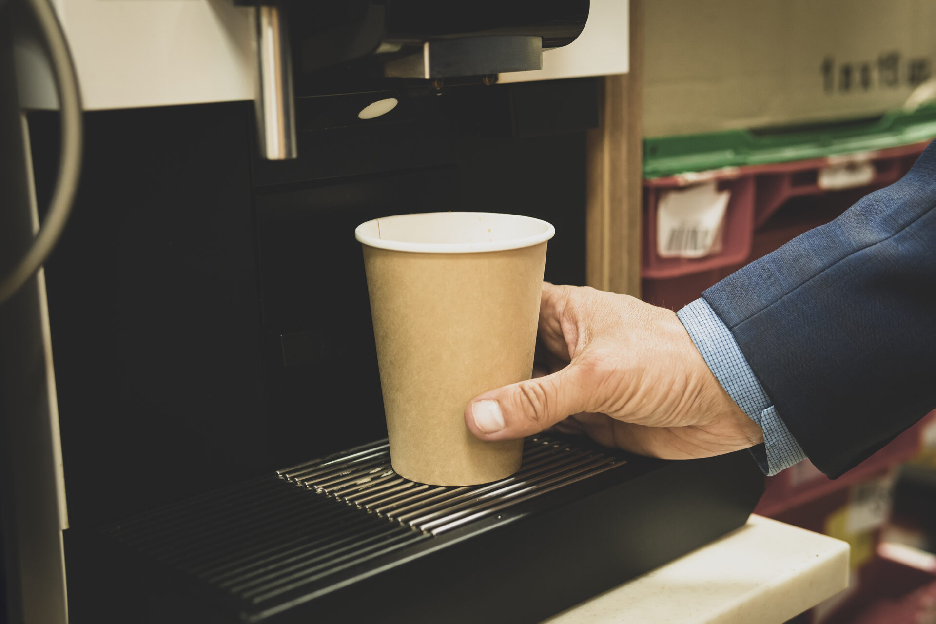 Hand placing cup under coffee machine.